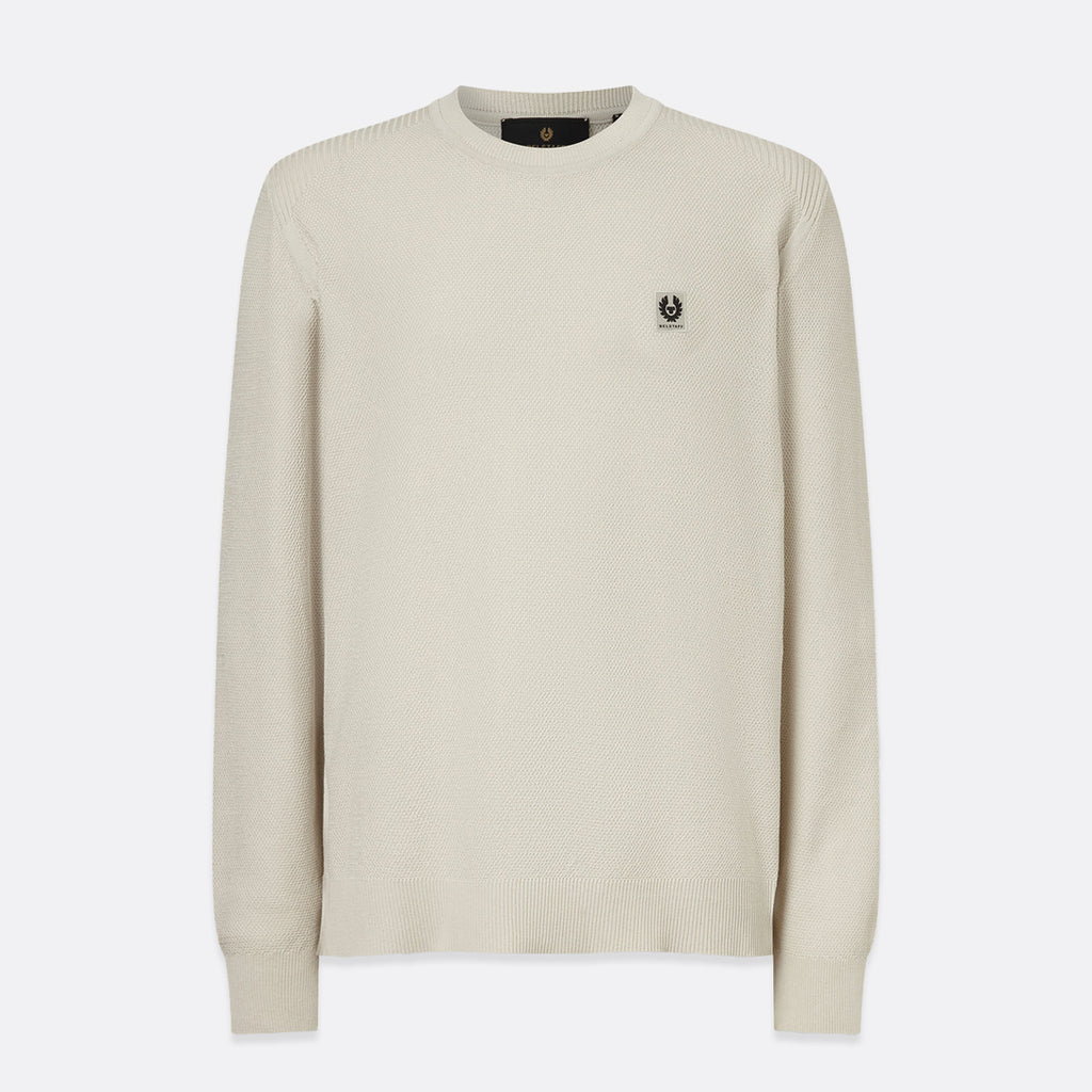 A cream-colored long-sleeve knit sweater with a small embroidered black logo on the left chest, displayed against a light gray background. Belstaff Sweatshirt. Sakks Menswear Southampton.