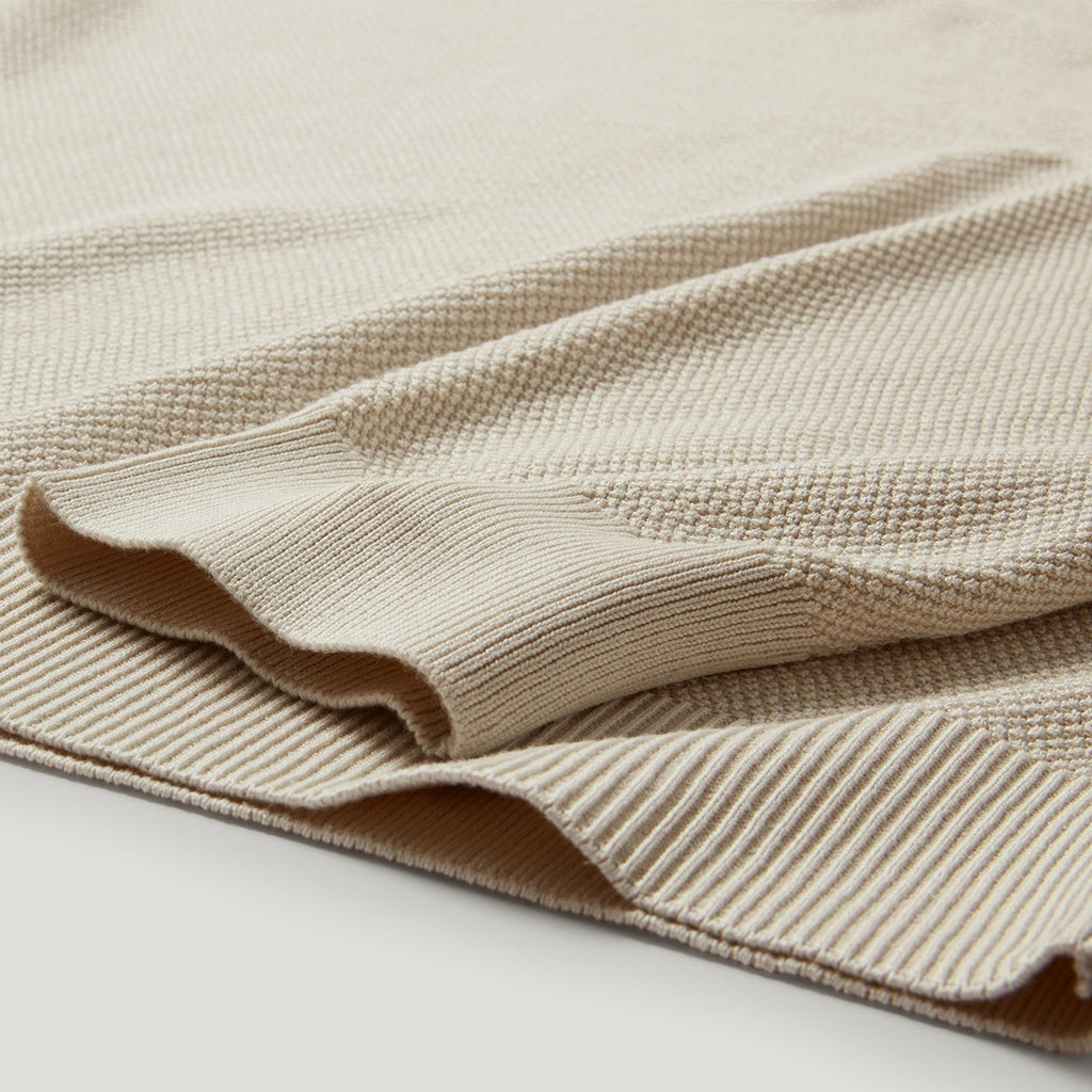 A close-up of a folded beige knit fabric with a textured waffle pattern and ribbed edges, shown on a light neutral background. Belstaff Sweatshirt. Sakks Menswear Southampton.