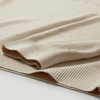 A close-up of a folded beige knit fabric with a textured waffle pattern and ribbed edges, shown on a light neutral background. Belstaff Sweatshirt. Sakks Menswear Southampton.