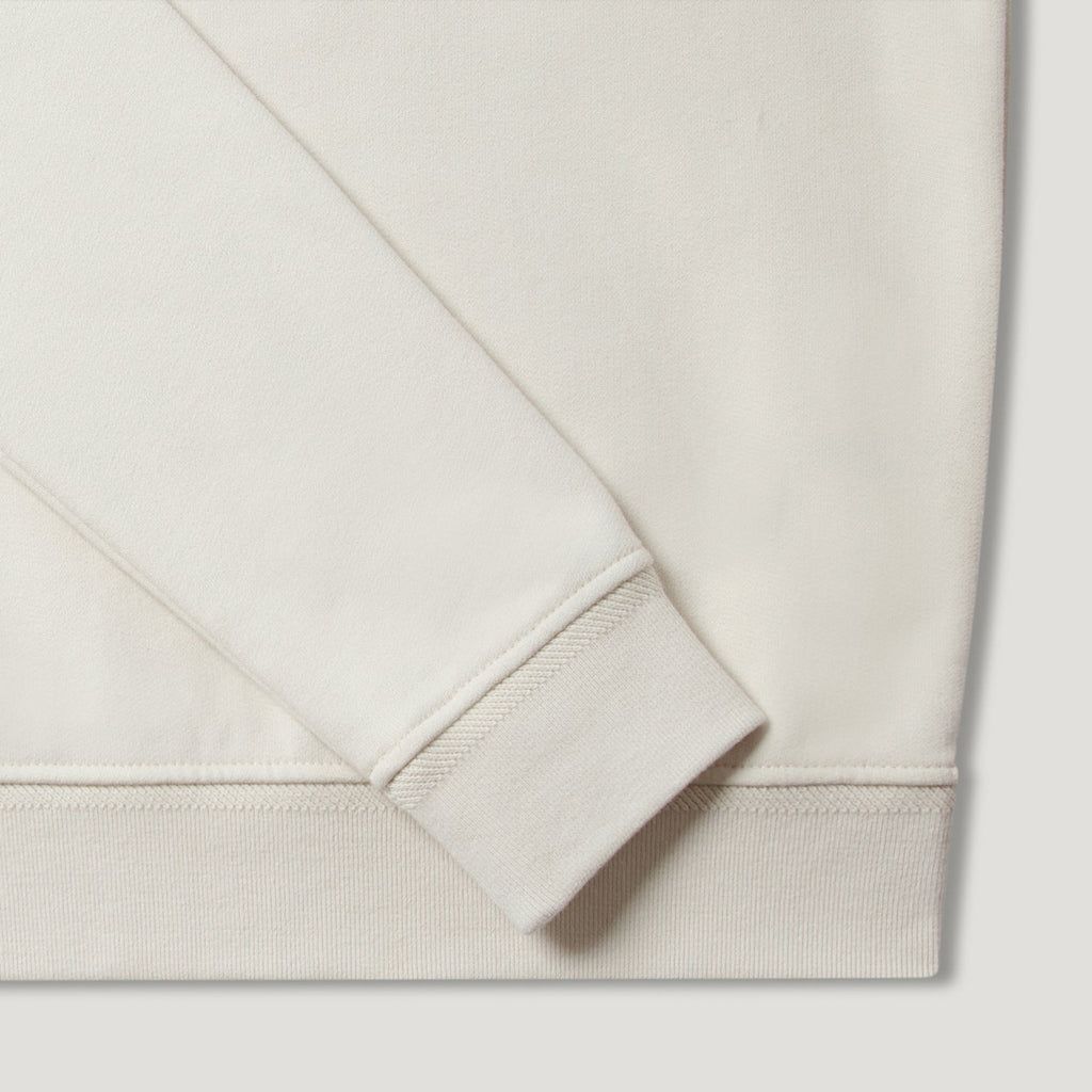 Close-up detail of a crewneck sweatshirt showing the sleeve cuff and ribbed hem in a warm off-white or cream colour. Belstaff Quarter Zip. Sakks Menswear Southampton.