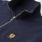 Close-up of a navy blue quarter-zip fleece jacket with a silver zipper and a black embroidered BELL STAFF logo patch on the chest. Belstaff Quarter Zip. Sakks Menswear Southampton.