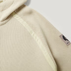 Close-up of a hooded sweatshirt in a light beige textured fabric, showing a pale yellow-green contrast stitched panel and a small black BELLA logo patch on the sleeve. Belstaff Hoodie. Sakks Menswear Southampton.