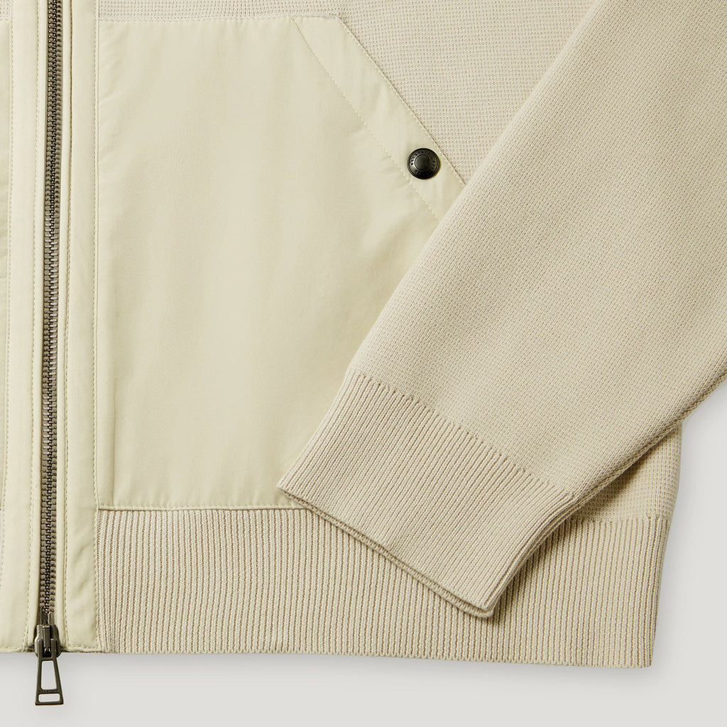 Close-up of a light beige jacket showing a smooth zippered panel, a ribbed knit sleeve, and a black snap button detail. Belstaff Hoodie. Sakks Menswear Southampton.