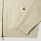 Close-up of a light beige jacket showing a smooth zippered panel, a ribbed knit sleeve, and a black snap button detail. Belstaff Hoodie. Sakks Menswear Southampton.