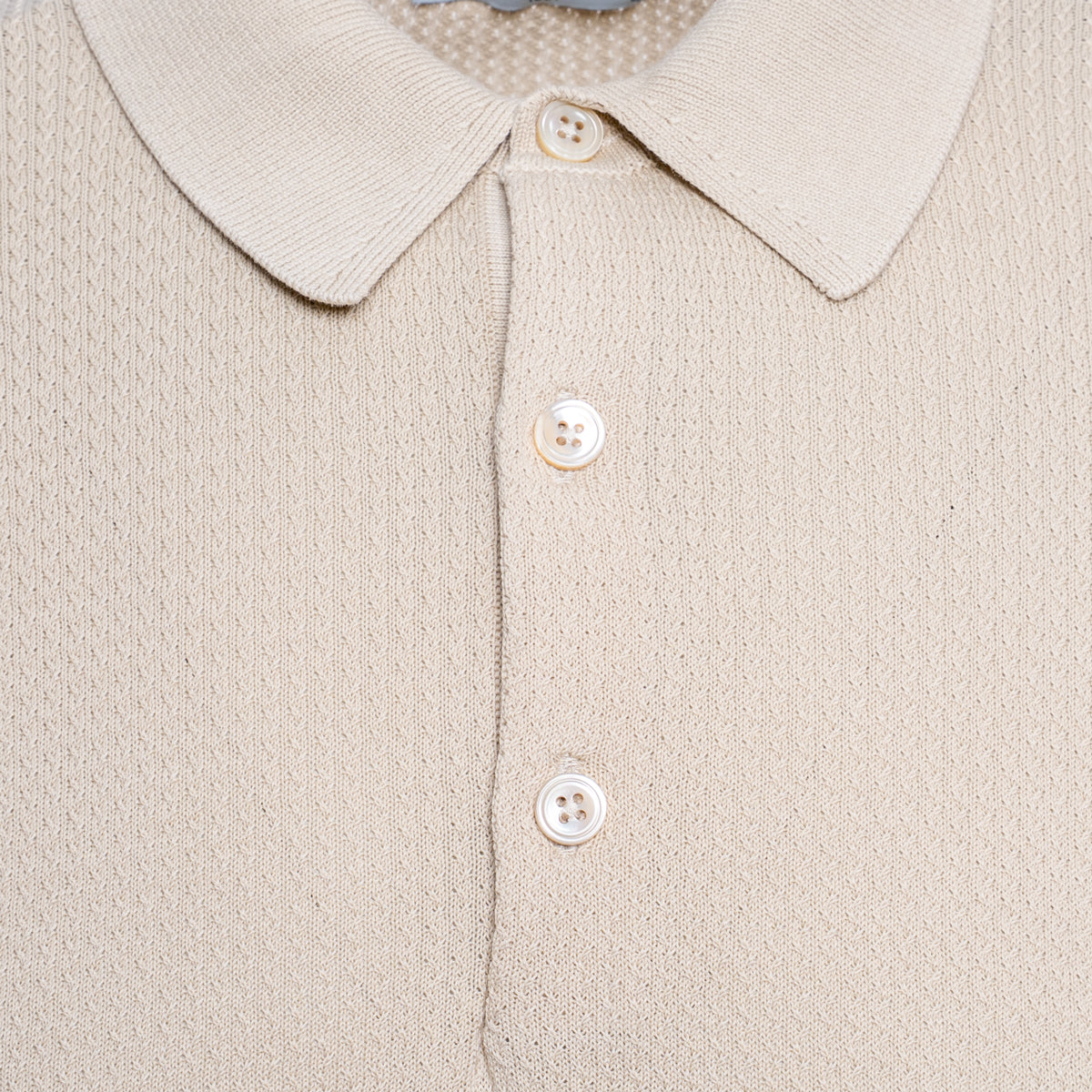 Close-up of a beige knit polo shirt showing the collar, three white buttons, and a fine textured fabric. Circolo 1901 Polo. Sakks Menswear Southampton.