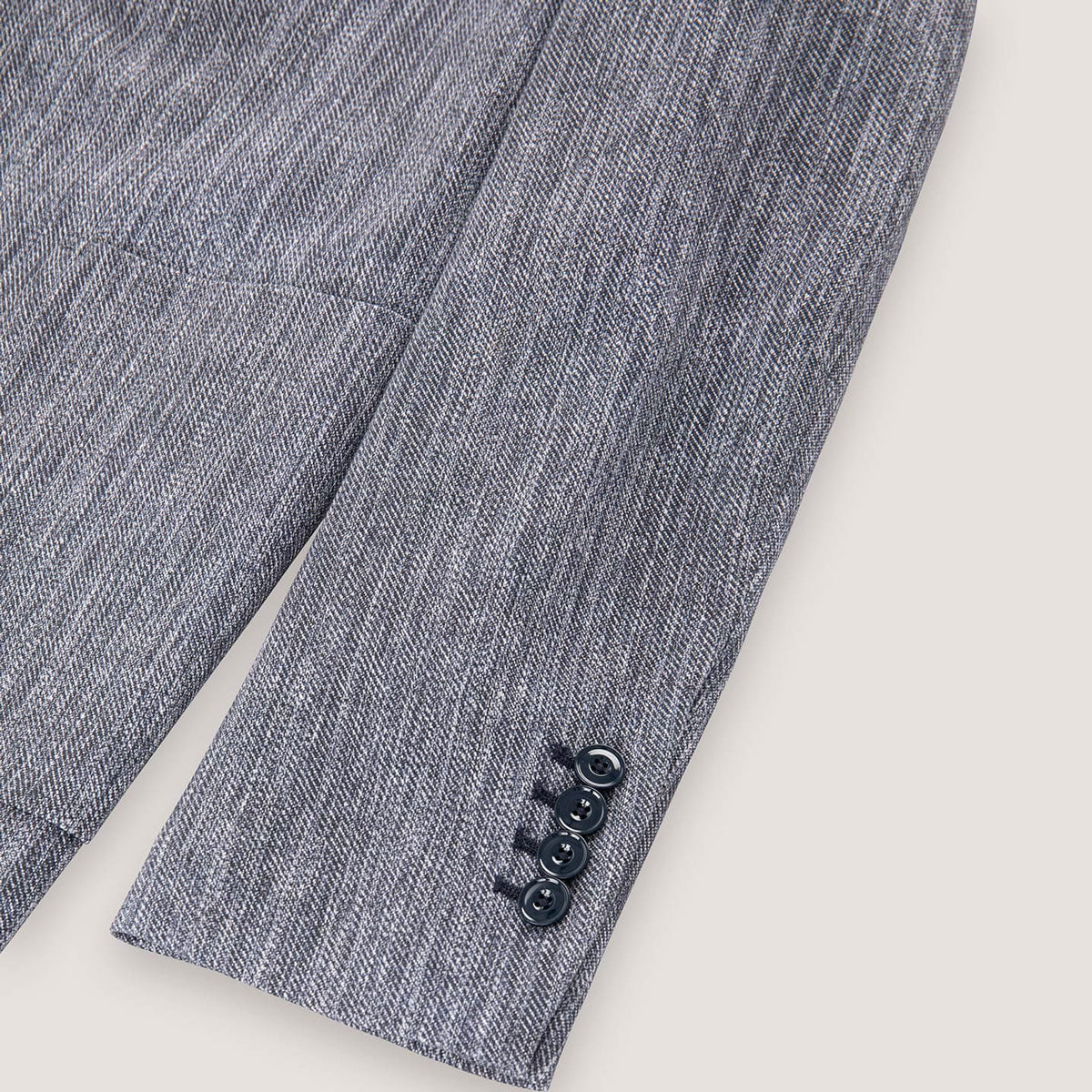 Close-up of a textured gray herringbone blazer sleeve showing three dark buttons on the cuff against a light beige background. Circolo 1901 Blazer. Sakks Menswear Southampton.