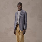 A man wearing a textured blue-gray blazer over a striped white shirt and beige trousers, standing against a beige patterned wall. Circolo 1901 Blazer. Sakks Menswear Southampton.