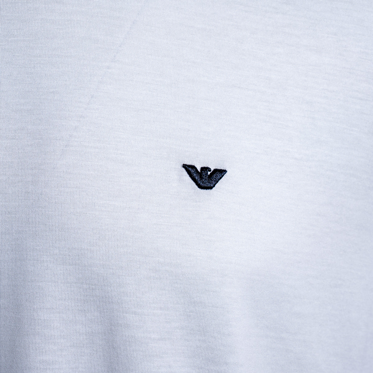 Close-up of a white heathered knit fabric with a small black embroidered Armani Privé logo centered on the chest. Emporio Armani T-Shirt. Sakks Menswear Southampton.