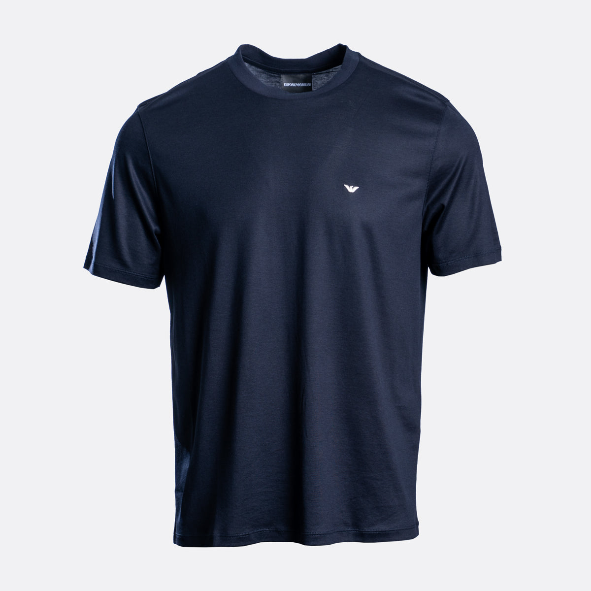 A navy blue short-sleeve crewneck t-shirt with a small white embroidered eagle logo on the left chest, displayed on a light gray background. Emporio Armani T-Shirt. Sakks Menswear Southampton.