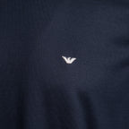Close-up of a dark navy blue knit fabric with a small white embroidered eagle logo at the center. Emporio Armani T-Shirt. Sakks Menswear Southampton.