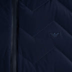 Close-up of a navy blue quilted jacket with a chevron pattern, a black zipper, and an embroidered dark logo on the chest. Emporio Armani Gilet. Sakks Menswear Southampton.