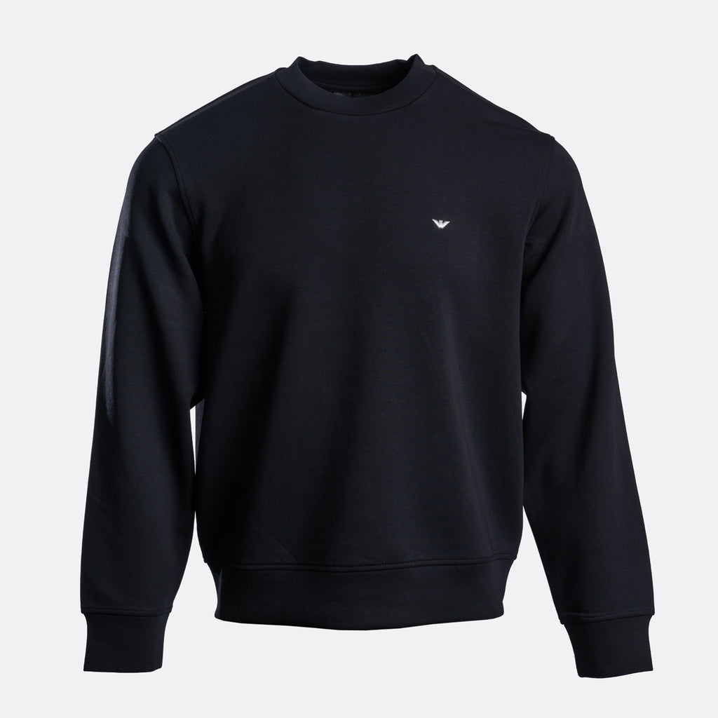 A black crewneck sweatshirt with a small white embroidered eagle logo on the left chest, displayed on a clean light gray background. Emporio Armani Sweatshirt. Sakks Menswear Southampton.