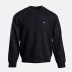 A black crewneck sweatshirt with a small white embroidered eagle logo on the left chest, displayed on a clean light gray background. Emporio Armani Sweatshirt. Sakks Menswear Southampton.