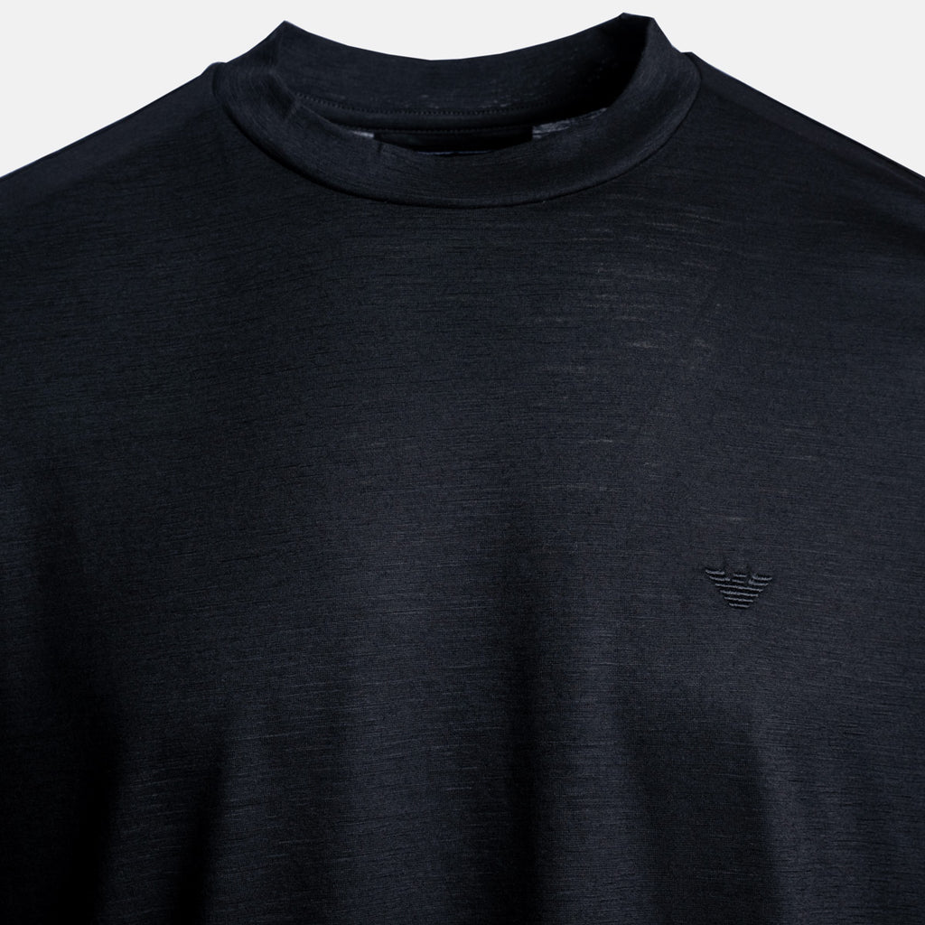 Close-up of a dark charcoal gray knit mock neck sweater with a subtle tonal embroidered logo on the left chest, set against a light gray background. Emporio Armani T-Shirt. Sakks Menswear Southampton.