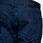 Close-up of the back waistband and right rear pocket of dark navy blue jeans, showing a black leather patch with 'EMPORIO ARMANI' text and a small embroidered logo on the pocket. Emporio Armani Chinos. Sakks Menswear Southampton.