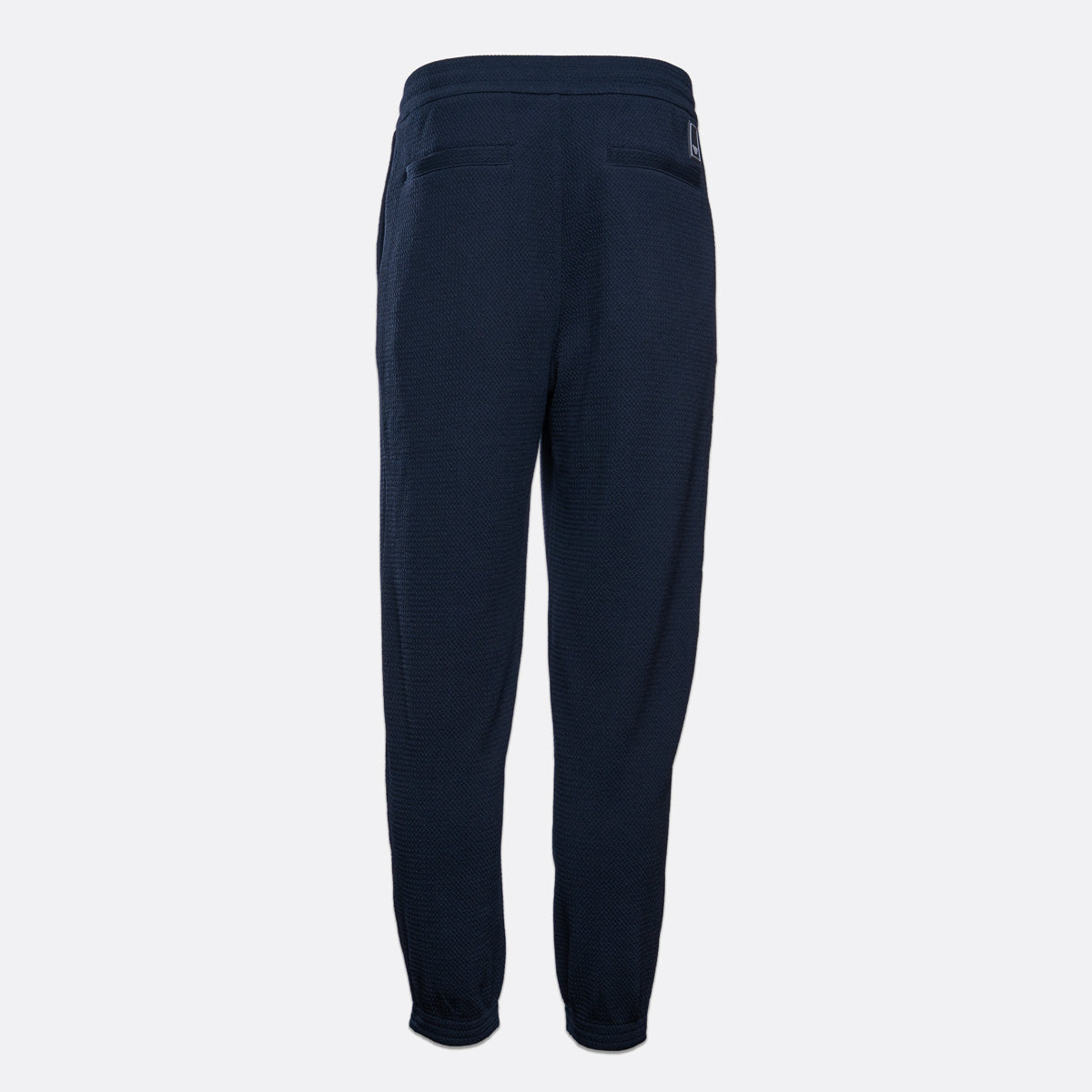 A pair of dark navy blue sweatpants shown from the back, featuring a relaxed fit and a small embroidered logo on the upper right side, set against a plain light gray background. Emporio Armani Sweat Pants. Sakks Menswear Southampton.