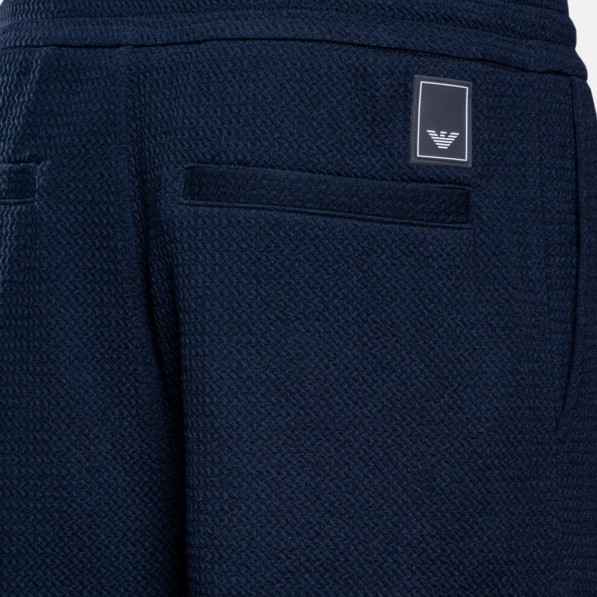 Close-up of navy blue textured fabric shorts showing a side pocket with a small rectangular Emporio Armani logo patch. Emporio Armani Sweat Pants. Sakks Menswear Southampton.