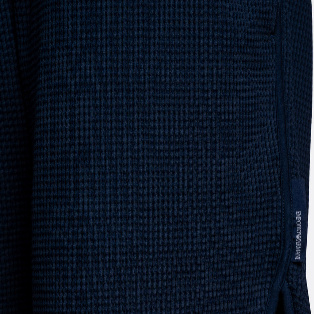 Close-up of a dark navy blue waffle-knit fabric with a small vertical woven brand tag reading EMPORIO ARMANI on the right side. Emporio Armani Shorts. Sakks Menswear Southampton.