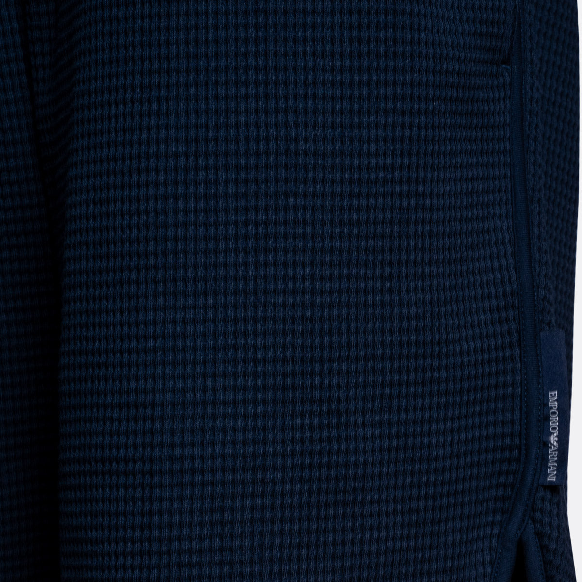 Close-up of a dark navy blue waffle-knit fabric with a small vertical woven brand tag reading EMPORIO ARMANI on the right side. Emporio Armani Shorts. Sakks Menswear Southampton.