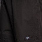 Close-up of a black lightweight jacket or overshirt fabric with a small rectangular brand patch near the lower hem. The patch shows the Armani Exchange eagle logo. Emporio Armani Shorts. Sakks Menswear Southampton.