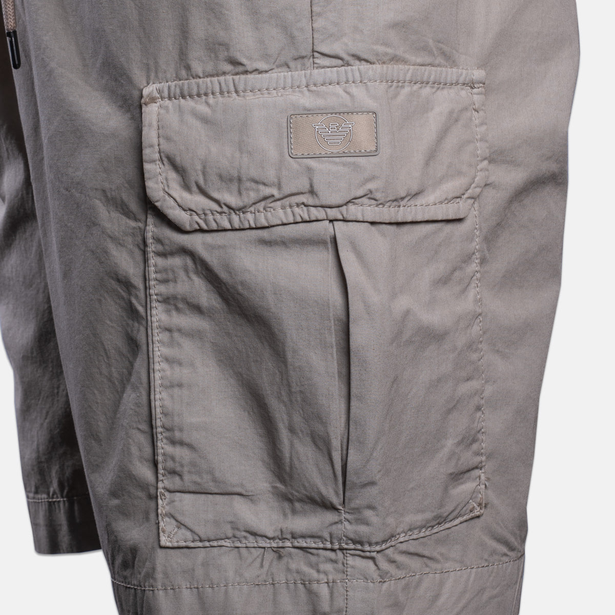 Close-up of a gray cargo-style jacket or overshirt showing a large front flap pocket with a small rectangular brand patch on the pocket. Emporio Armani Shorts. Sakks Menswear Southampton.