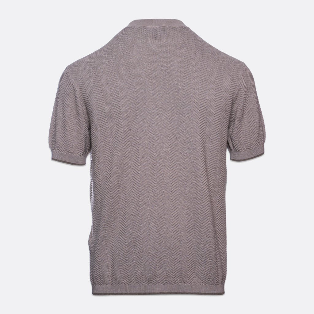 A short-sleeve knit polo shirt shown from the back, featuring a textured chevron pattern in a muted taupe-gray color, set against a plain light gray background. Emporio Armani T-Shirt. Sakks Menswear Southampton.