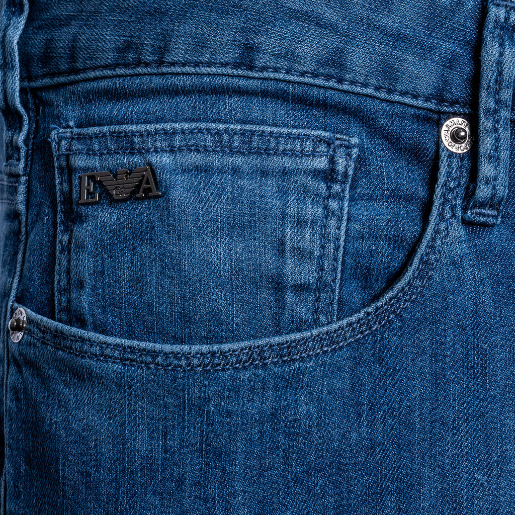 Close-up of a blue denim jeans pocket showing the black embroidered Emporio Armani logo patch and silver metal rivets. Emporio Armani Jeans. Sakks Menswear Southampton.