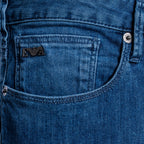 Close-up of a blue denim jeans pocket showing the black embroidered Emporio Armani logo patch and silver metal rivets. Emporio Armani Jeans. Sakks Menswear Southampton.