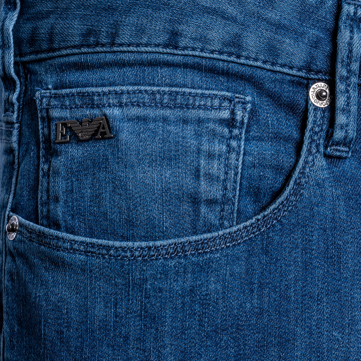 Close-up of a blue denim jeans pocket showing the black embroidered Emporio Armani logo patch and silver metal rivets. Emporio Armani Jeans. Sakks Menswear Southampton.
