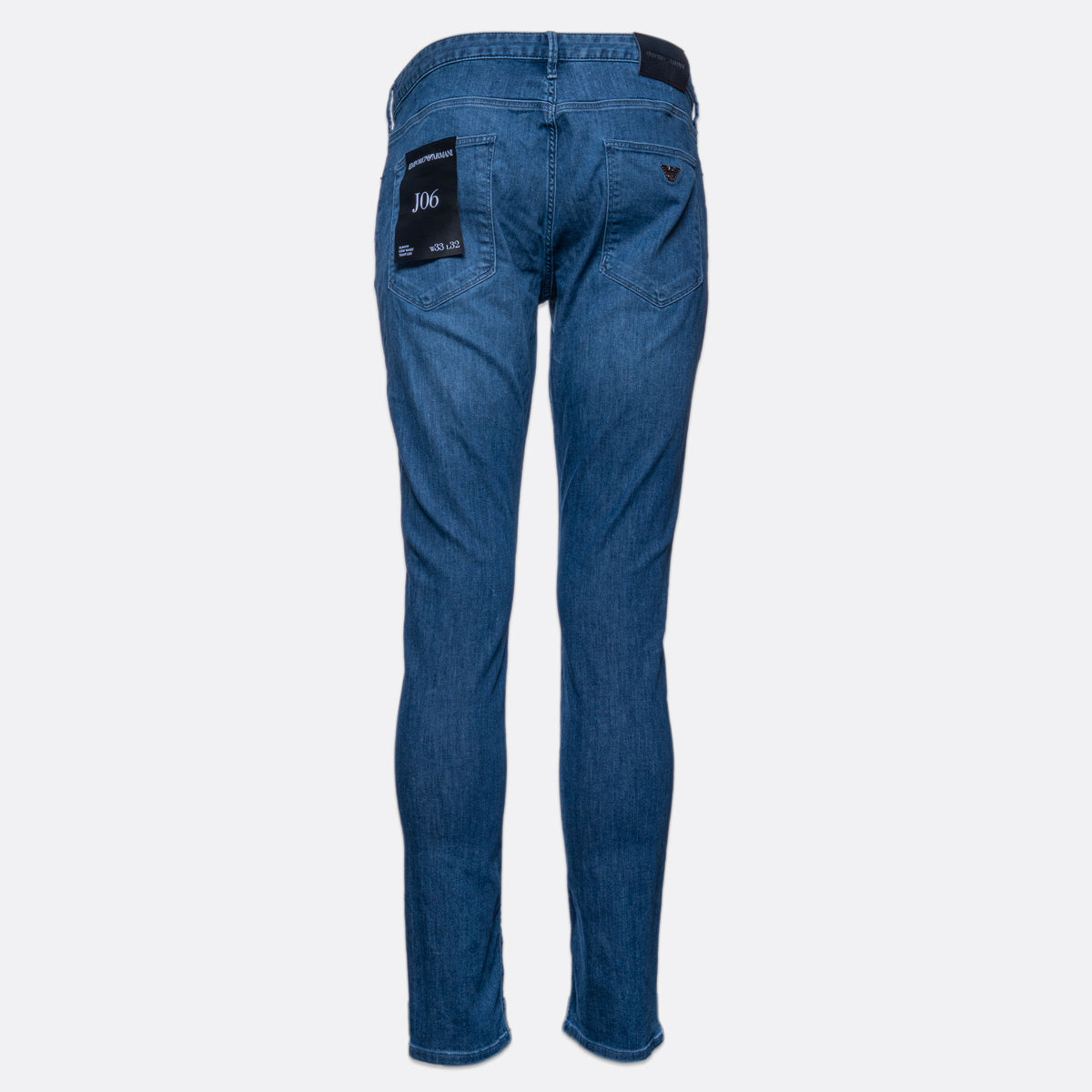 Blue denim jeans shown from the back, featuring a black brand patch on the right pocket and a small embroidered logo on the left pocket, set against a plain light gray background. Emporio Armani Jeans. Sakks Menswear Southampton.