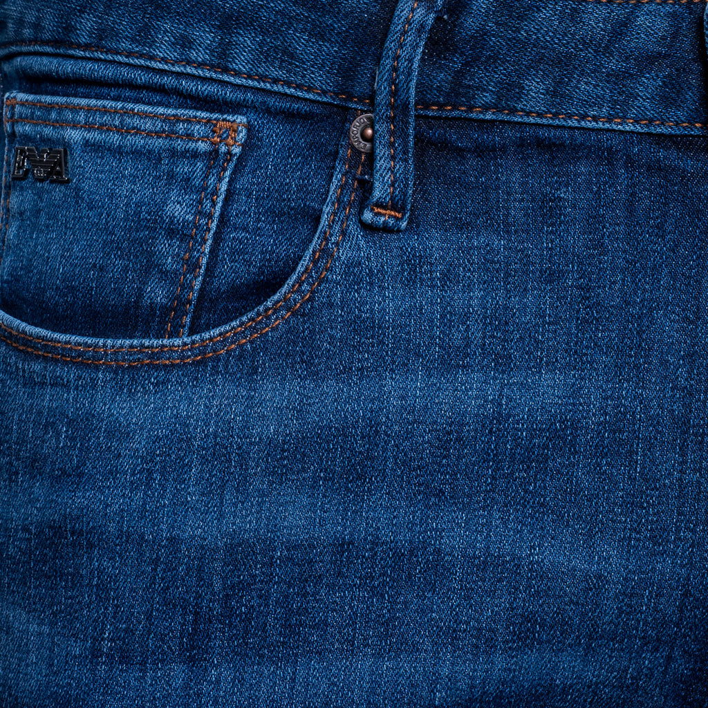 Close-up of the back pocket and waistband of blue denim jeans, showing stitching, a metal rivet, and a small black brand patch on the pocket. Emporio Armani Jeans. Sakks Menswear Southampton.