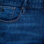 Close-up of the back pocket and waistband of blue denim jeans, showing stitching, a metal rivet, and a small black brand patch on the pocket. Emporio Armani Jeans. Sakks Menswear Southampton.