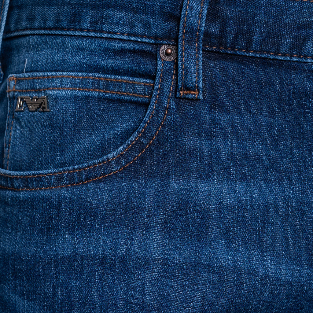 Close-up of dark blue denim jeans showing the back pocket with contrast stitching and a small metal logo patch. Emporio Armani Jeans. Sakks Menswear Southampton.