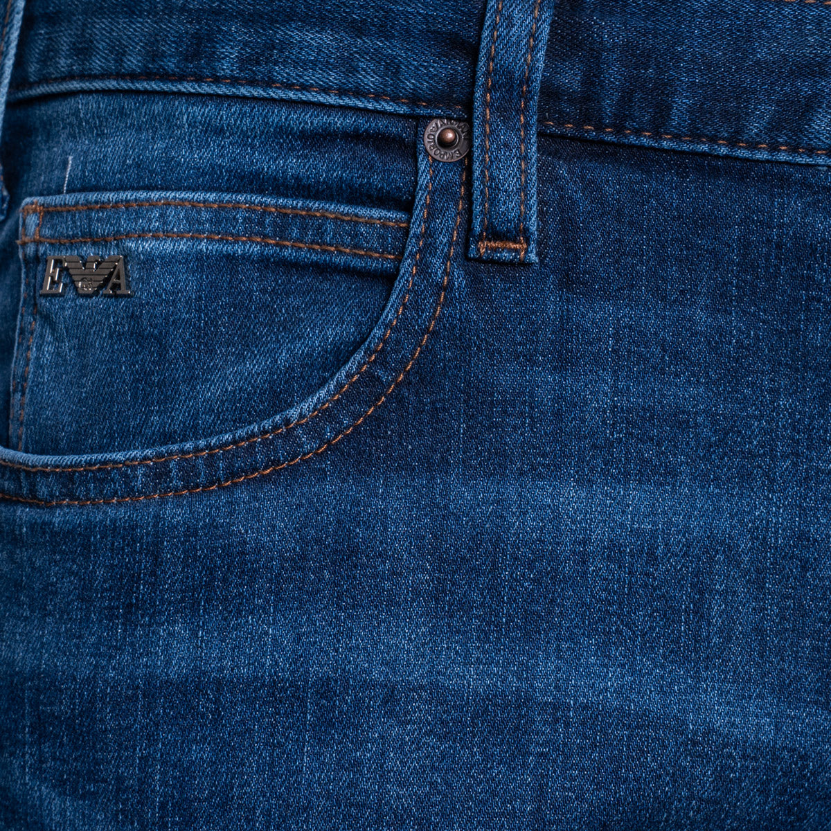 Close-up of dark blue denim jeans showing the back pocket with contrast stitching and a small metal logo patch. Emporio Armani Jeans. Sakks Menswear Southampton.