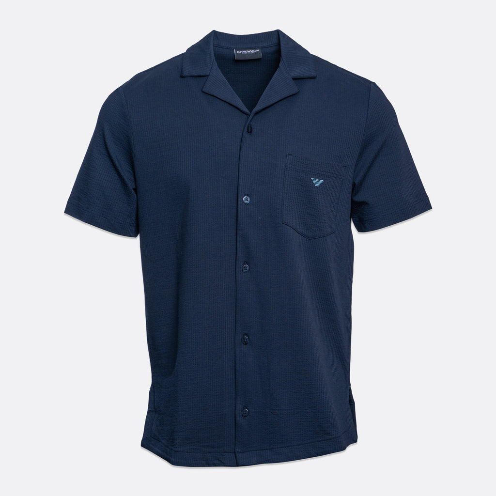 A navy blue short-sleeve button-up shirt with a camp collar, featuring a left chest pocket with a small embroidered logo and a subtle textured weave, shown on a light gray background. Emporio Armani Short Sleeve Shirt. Sakks Menswear Southampton.