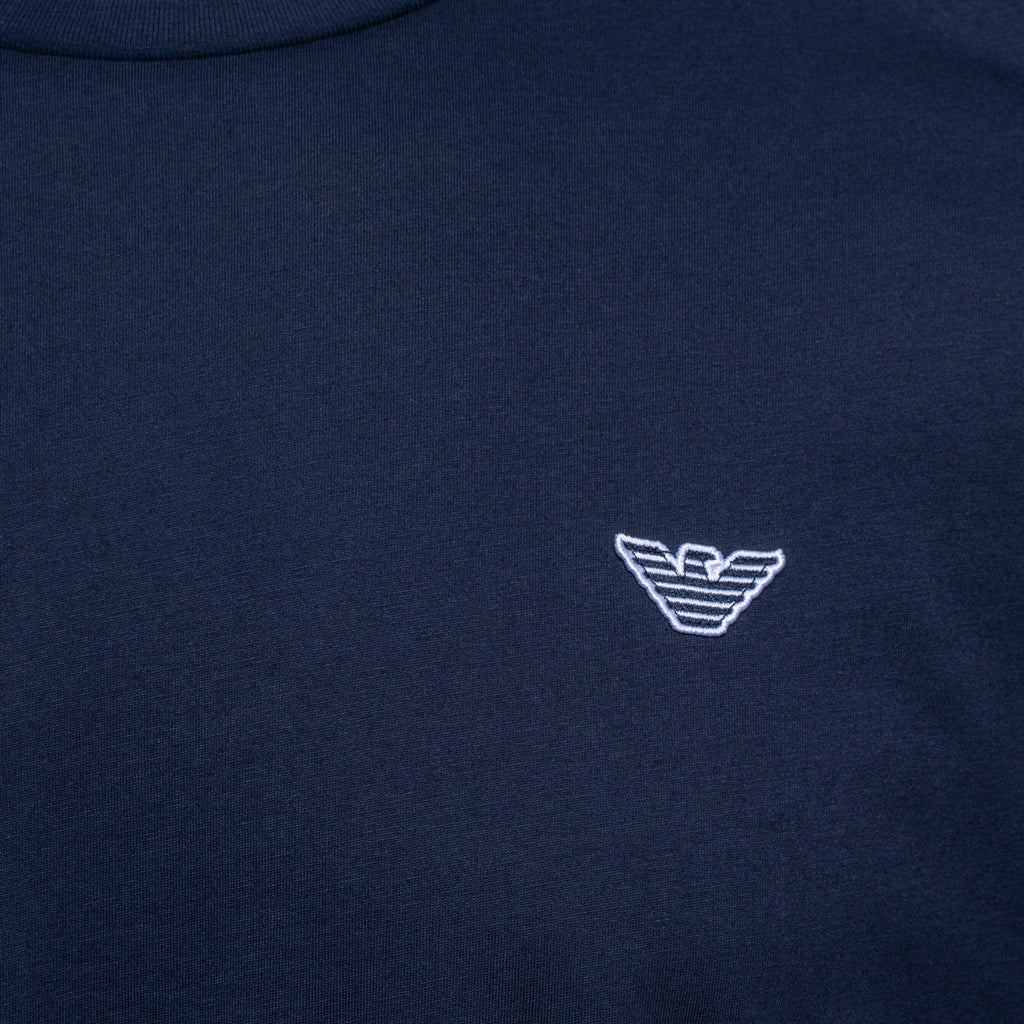 Close-up of a navy blue crewneck sweatshirt featuring the white embroidered logo of Emporio Armani on the chest. Emporio Armani T-Shirt. Sakks Menswear Southampton.
