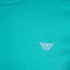 Close-up of a turquoise knit fabric with a small white embroidered Emporio Armani eagle logo on the chest. Emporio Armani T-Shirt. Sakks Menswear Southampton.