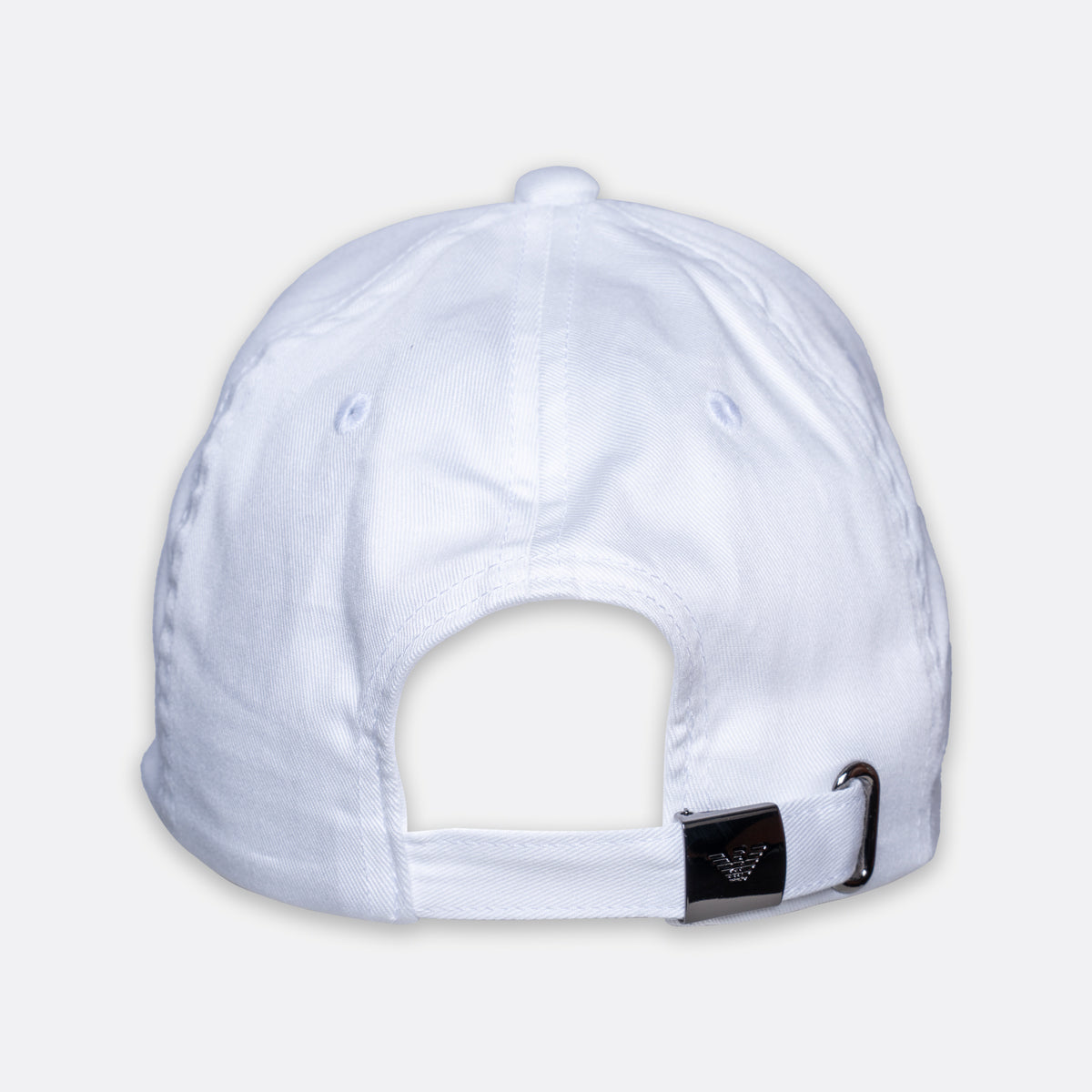 White baseball cap shown from the back, featuring a fabric strap closure with a black square patch and silver metal buckle, set against a light gray background. Emporio Armani Cap. Sakks Menswear Southampton.