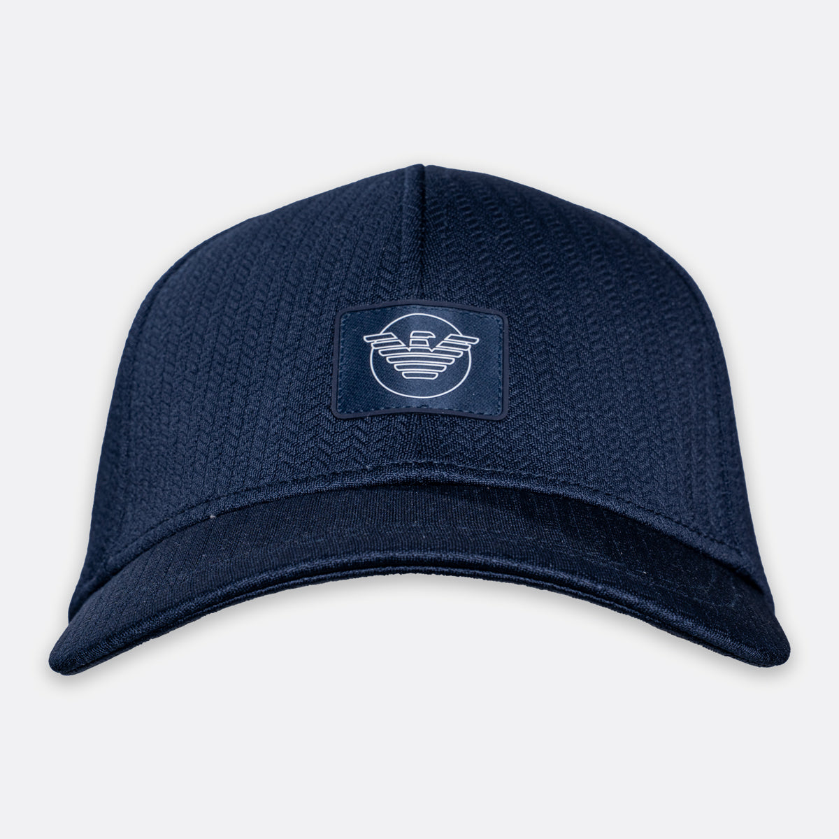 A navy blue structured baseball cap with a textured herringbone pattern, featuring a rectangular patch on the front with a white stylized logo. Emporio Armani Cap. Sakks Menswear Southampton