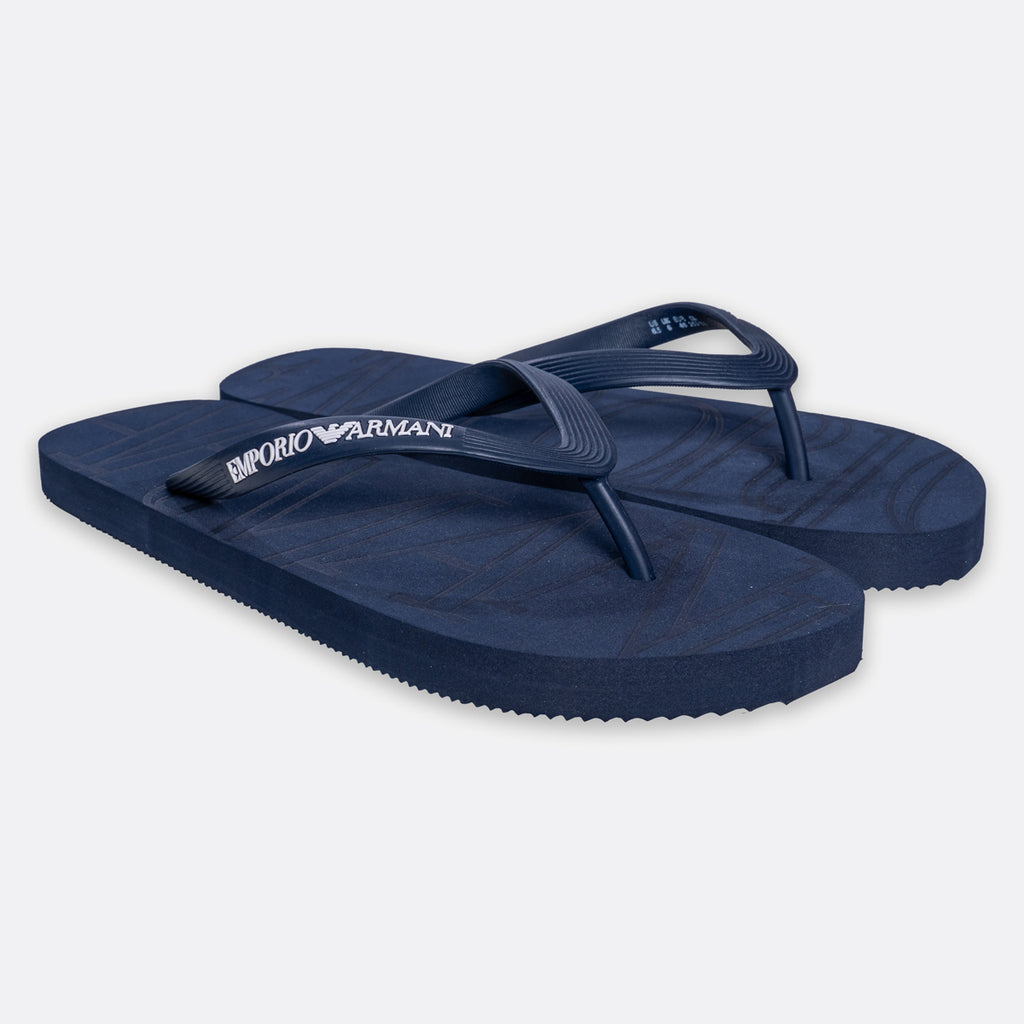 A pair of navy blue Armani Exchange flip-flops with the brand name printed in white on the strap, set against a light gray background. Emporio Armani Flip Flops. Sakks Menswear Southampton.