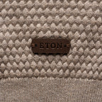 Close-up of a textured knit sweater in taupe and cream with a dark brown leather patch on the chest reading 'ETON'. Eton Knitwear available at Sakks Menswear in Southampton.