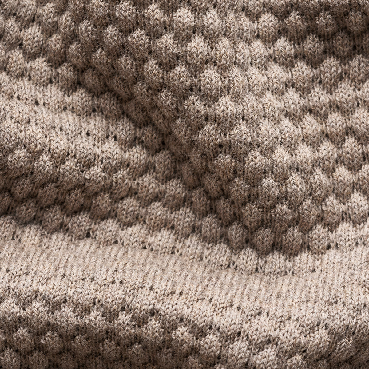 Close-up of a knitted textile with a textured honeycomb pattern in taupe and beige tones, showing the fabric weave and ribbed border. Eton Knitwear available at Sakks Menswear in Southampton.