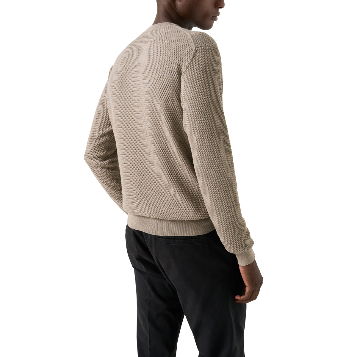 A man wearing a textured beige knit sweater and black trousers, shown from a side-back angle against a plain white background. Eton Knitwear available at Sakks Menswear in Southampton.