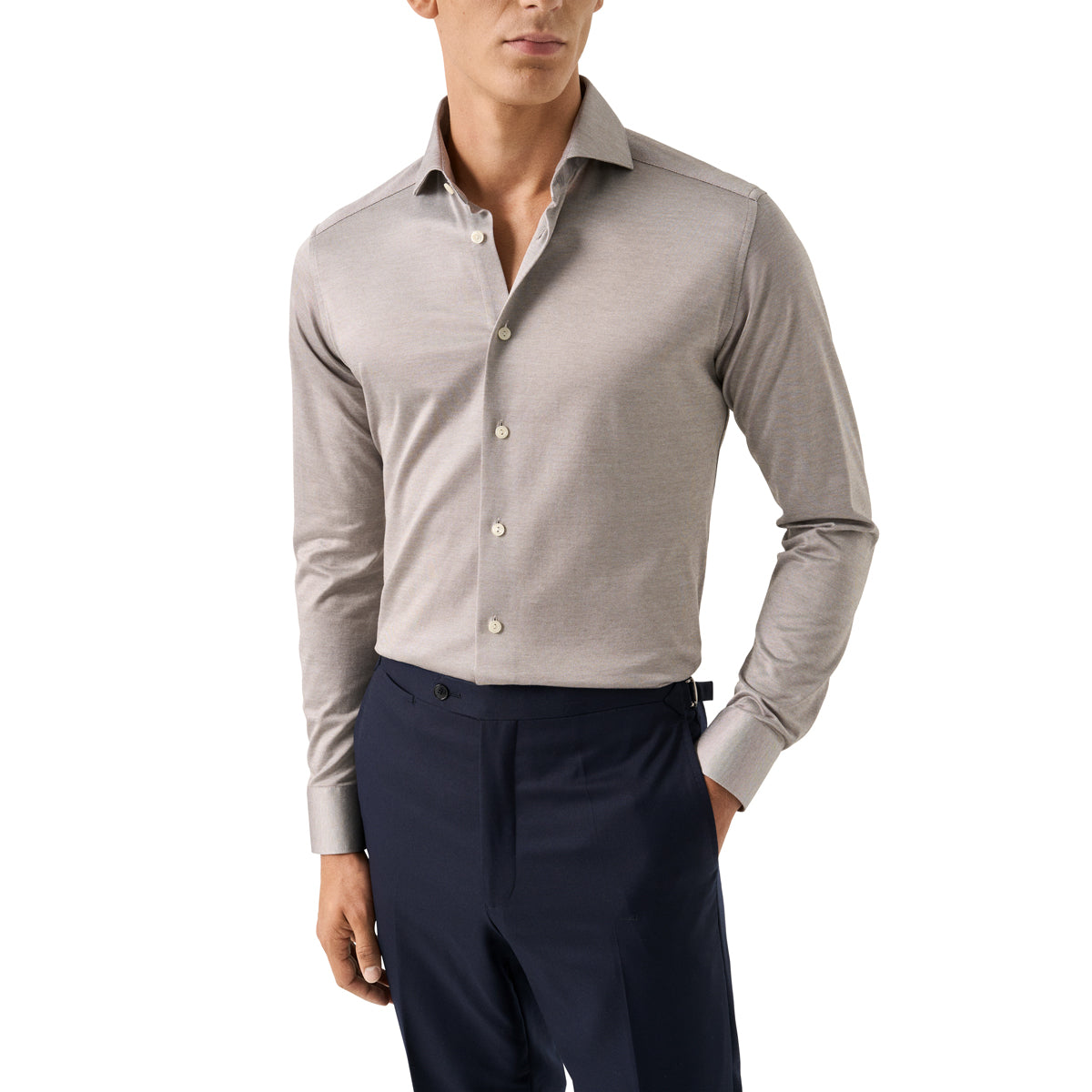 A man wearing a light taupe-beige long-sleeve button-down dress shirt tucked into dark navy trousers, shown from the chin down against a plain white background. Eton Shirt available at Sakks Menswear in Southampton.