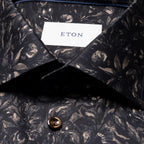 Close-up of a dark patterned ETON button-down shirt collar with a white neck label and a brown button. Eton Shirt available at Sakks Menswear in Southampton.