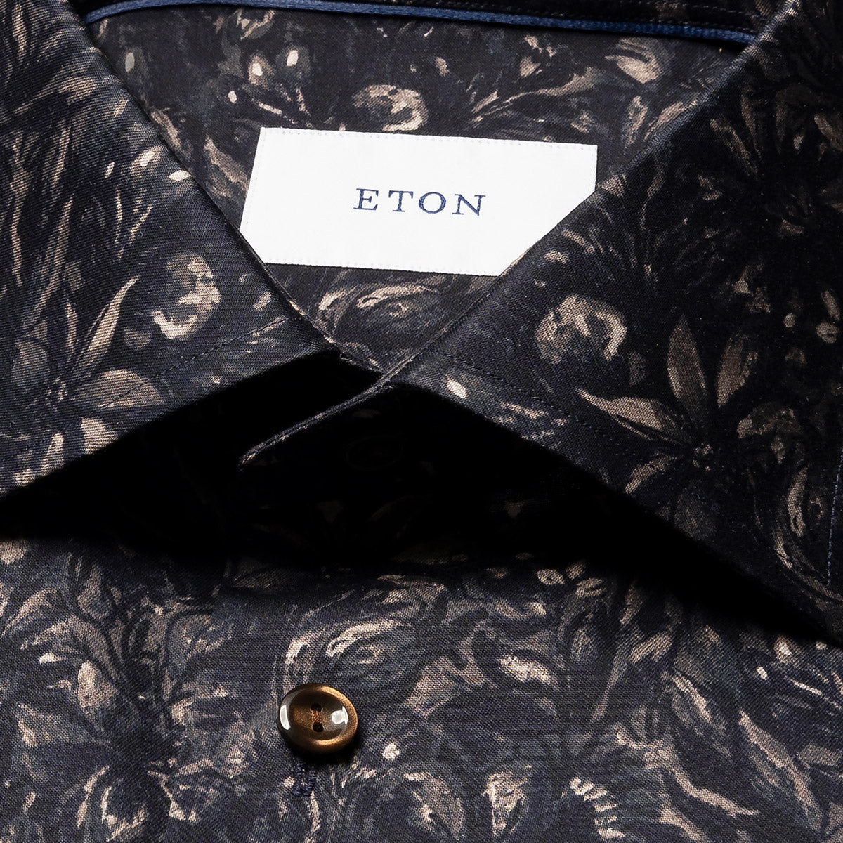 Close-up of a dark patterned ETON button-down shirt collar with a white neck label and a brown button. Eton Shirt available at Sakks Menswear in Southampton.