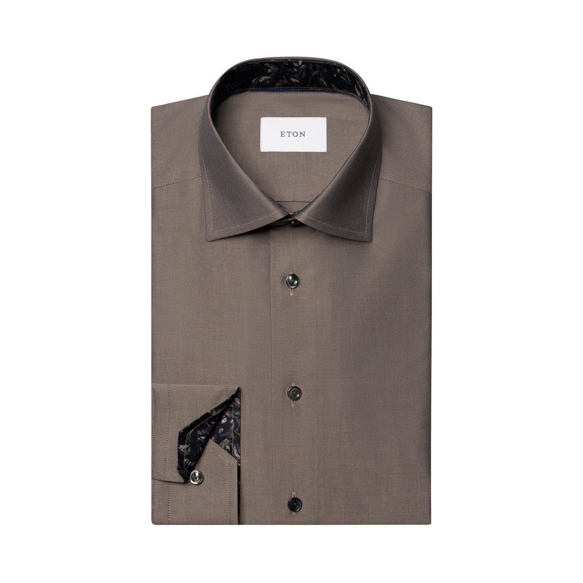 A folded brown dress shirt with a pointed collar, dark buttons, and a black patterned inner collar and pocket square, shown on a plain white background. The neck label reads ETON. Eton Shirt available at Sakks Menswear in Southampton.