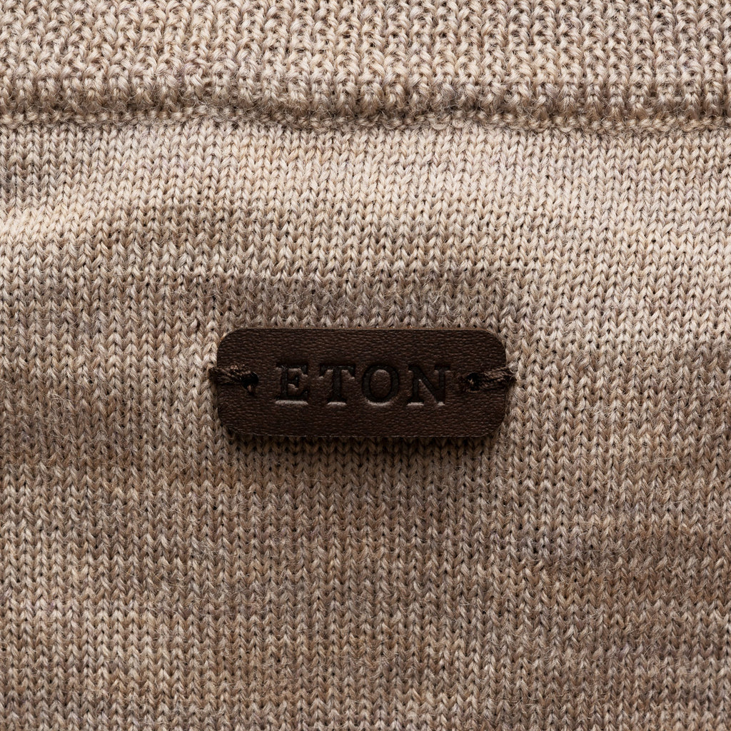 Close-up of a beige knit sweater with a dark brown leather patch on the back reading 'ETON' in raised letters. Eton Cardigan available at Sakks Menswear in Southampton.