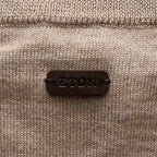 Close-up of a beige knit sweater with a dark brown leather patch on the back reading 'ETON' in raised letters. Eton Cardigan available at Sakks Menswear in Southampton.