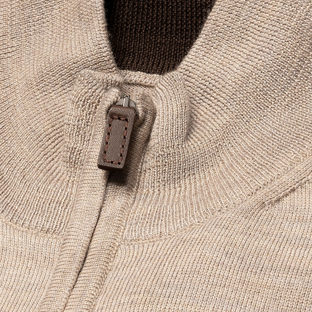 Close-up of a ribbed knit sweater in a light oatmeal beige colour, featuring a brown leather pull tab on the zipper. Eton Cardigan available at Sakks Menswear in Southampton.